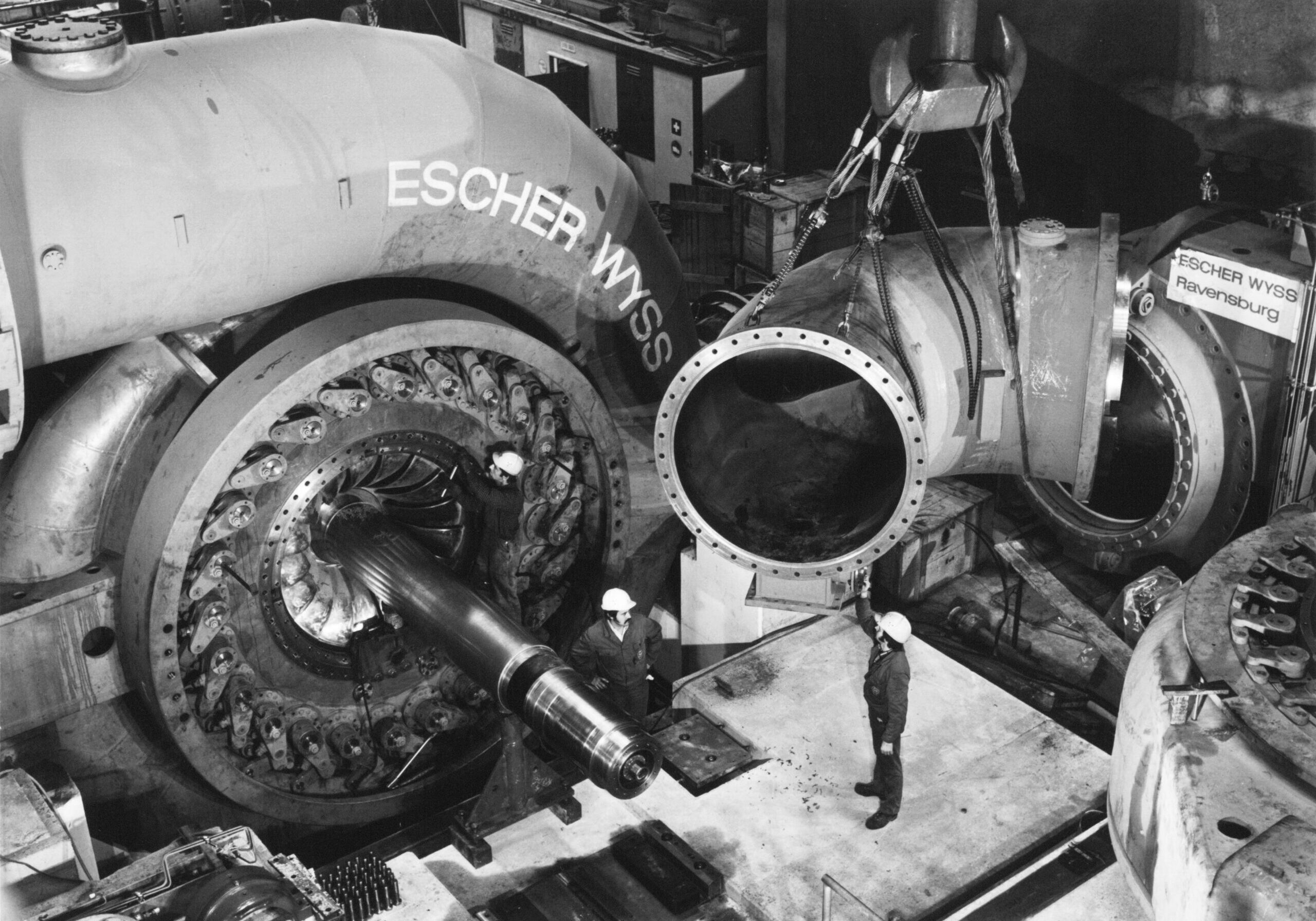 Der Saugkrümmer einer der vier Francis-Spiralturbinen des Pumpspeichers Wehr wird mit dem Maschinenhauskran in Position gehoben. Zwei Mitarbeiter helfen am Boden mit.